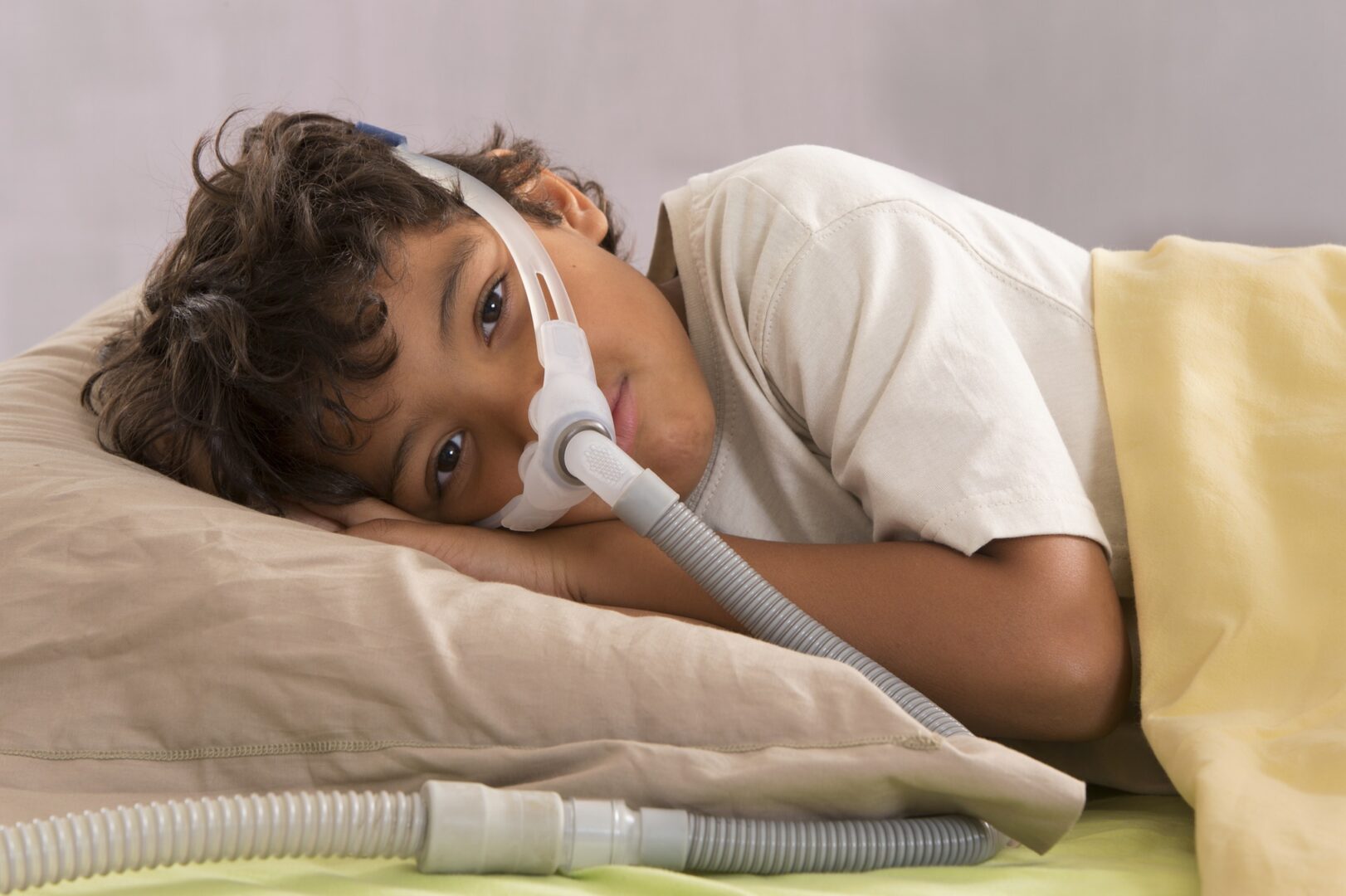 A young boy laying in bed with an electric toothbrush.