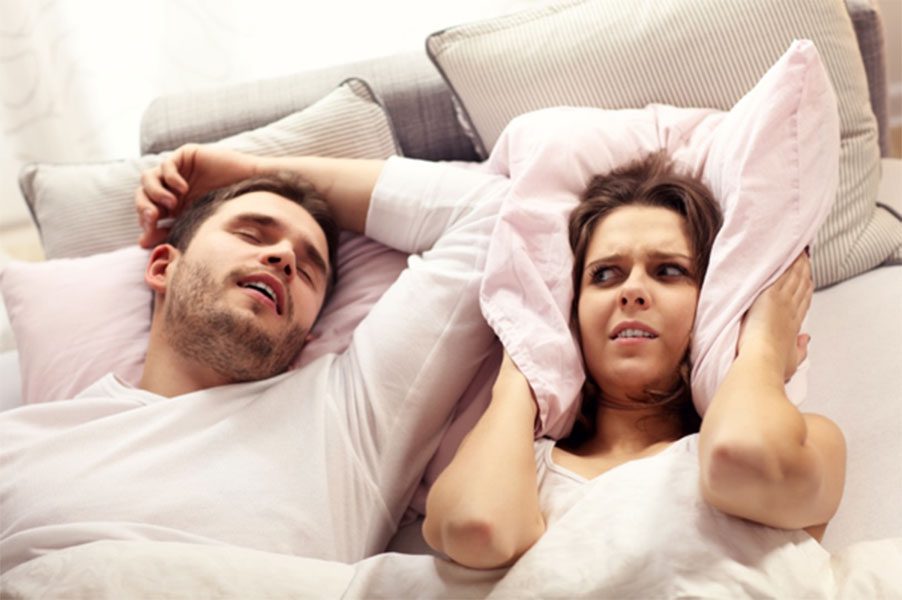 A man and woman laying in bed with pillows.